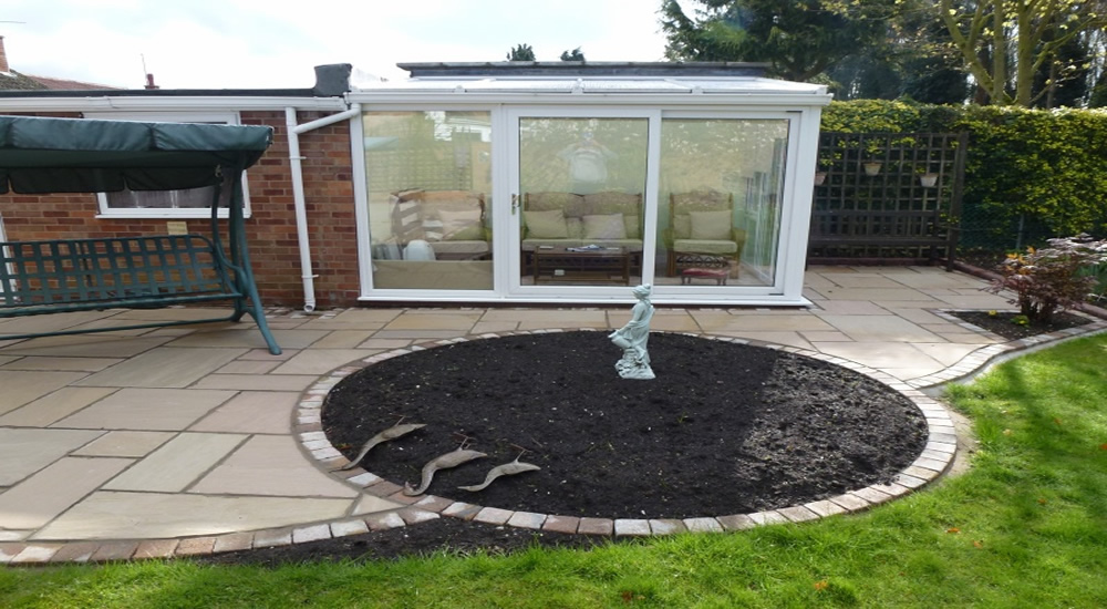 Sandstone patio wrapping a circular planted bed with brick edging